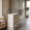Muniq artificial stone pedestal basin 1329 400x850mm showing warm cream square monolith with organic horizontal sandstone strata layered texture on lower pedestal and smooth integrated square bowl