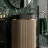 Muniq artificial stone pedestal basin 1341 600x375x850mm showing warm sand fluted oval column pedestal with matte black oval bowl and precision gold ring against dark green wall with planting