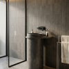 Muniq concrete drum basin charcoal grey freestanding pedestal sink with wide flat rim drum bowl and narrow cylinder column in industrial luxury bathroom with dark tile wall and matte black tap