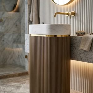 Muniq artificial stone pedestal basin 1343 600x375x850mm showing warm bronze tan fluted oval column pedestal with clean white oval bowl and precision gold ring accent classical luxury washbasin