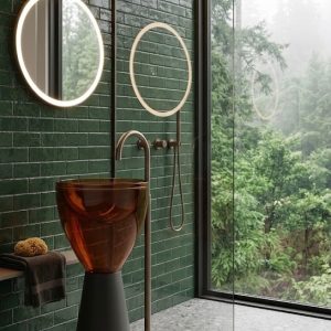 Freestanding amber cognac transparent resin bowl basin 7104 with wide glowing amber bowl on dark charcoal cone pedestal and slim gold floor faucet in luxury bathroom with mountain view