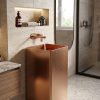 Brushed copper freestanding stainless steel square pedestal basin with warm rose copper PVD finish and water flowing from copper wall-mounted faucet in travertine bathroom