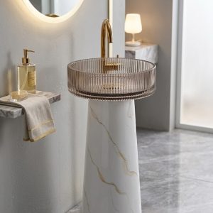 Muniq Statvario resin freestanding basin with fluted crystal bowl showing white gold marble effect tapered pedestal and transparent ribbed resin bowl with polished gold tap in warm luxury bathroom with LED mirror
