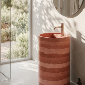 Eclipse freestanding concrete cylinder pedestal basin SNK40 in Rammed Earth colour with warm terracotta and rust horizontal stripe banding and rose gold faucet in bright luxury bathroom
