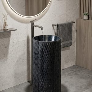 Black composite stone freestanding chiselled pedestal basin with raw hand-textured exterior and polished dark interior bowl in warm stone contemporary bathroom